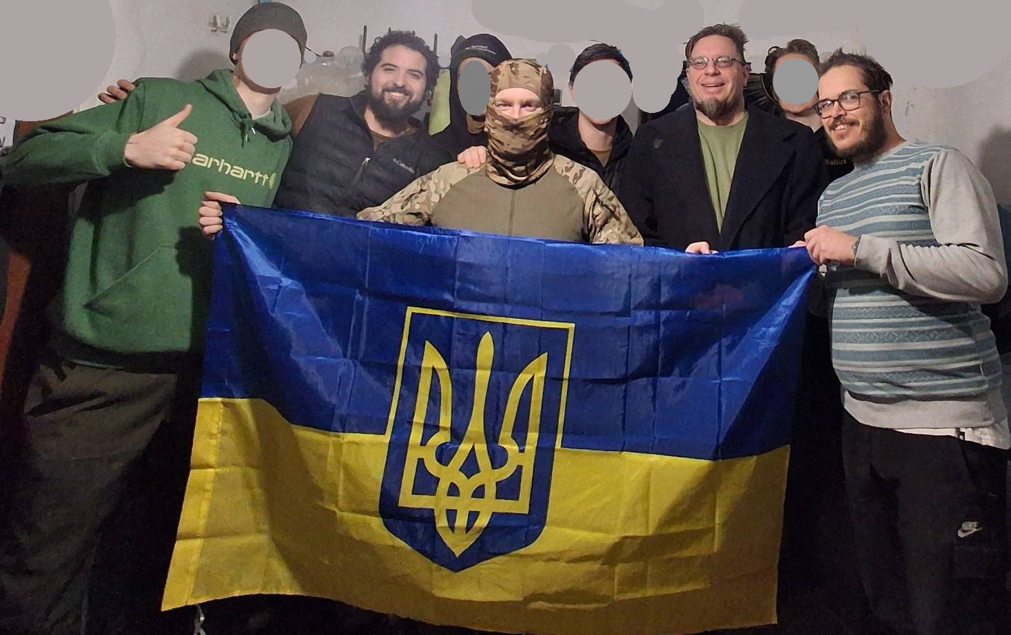 Group of people holding a Ukrainian flag with a stylized yellow and blue emblem.